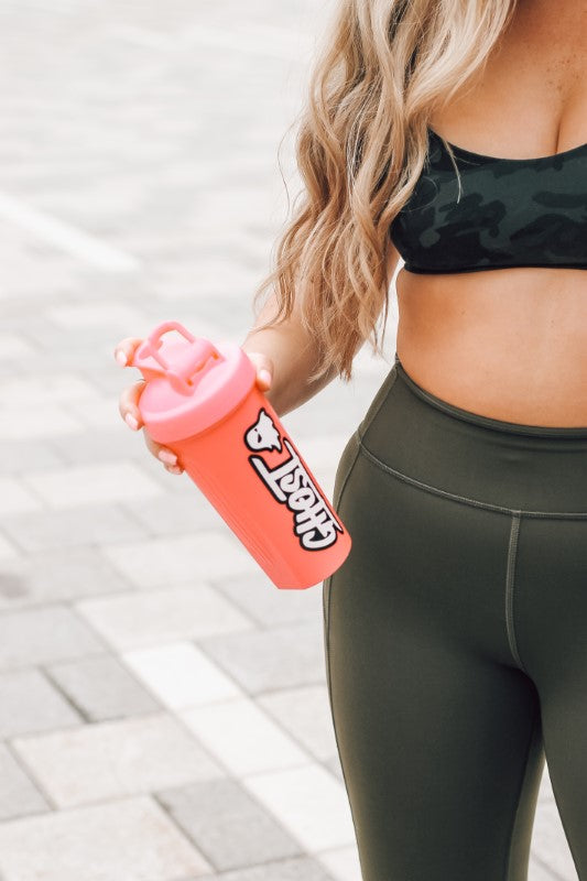 Mujer con vaso mezclador para proteínas en la mano, lista para hacer deporte