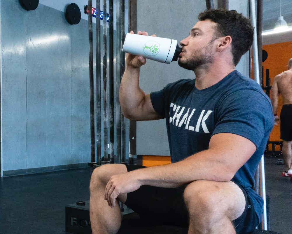 Hombre bebiendo de vaso mezclador su batido de proteínas en el gimnasio